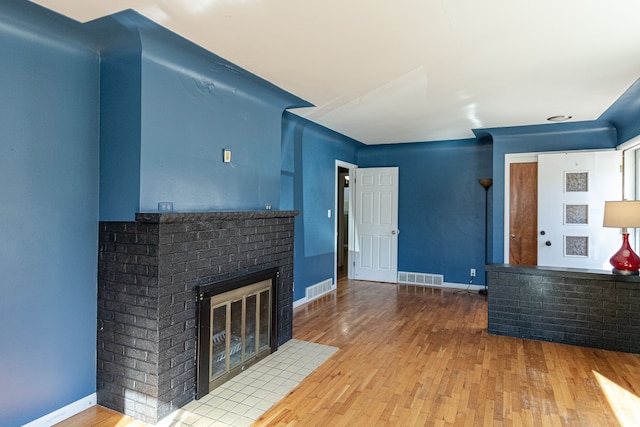 unfurnished living room with wood-type flooring and a brick fireplace