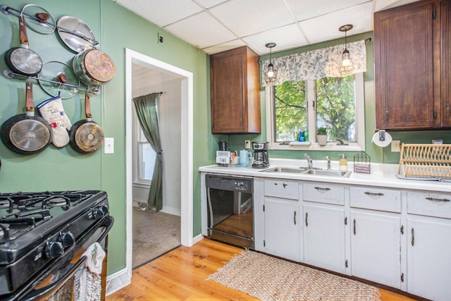 kitchen with a drop ceiling, sink, black appliances, light hardwood / wood-style floors, and hanging light fixtures