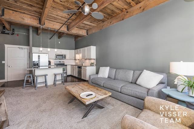 carpeted living room with wood ceiling, ceiling fan, sink, beam ceiling, and a high ceiling