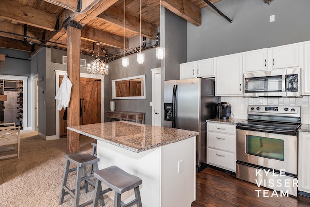 kitchen with appliances with stainless steel finishes, a towering ceiling, wooden ceiling, beamed ceiling, and white cabinetry