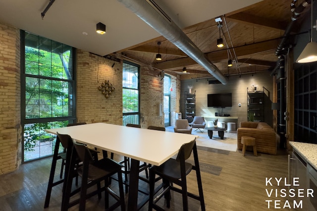 dining space featuring wood-type flooring, beam ceiling, a high ceiling, and brick wall