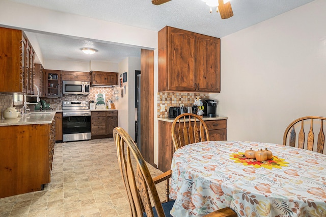 kitchen with decorative backsplash, a textured ceiling, stainless steel appliances, ceiling fan, and sink