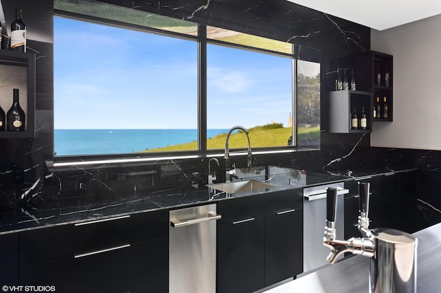 kitchen with a water view, tasteful backsplash, dark stone counters, and sink