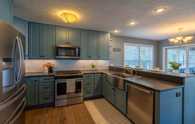 kitchen with kitchen peninsula, appliances with stainless steel finishes, decorative light fixtures, and hardwood / wood-style floors