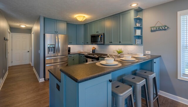 kitchen with a healthy amount of sunlight, dark hardwood / wood-style flooring, kitchen peninsula, and appliances with stainless steel finishes