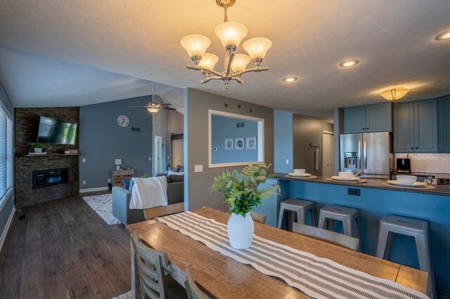 dining space with lofted ceiling, dark wood-type flooring, ceiling fan with notable chandelier, a textured ceiling, and a fireplace