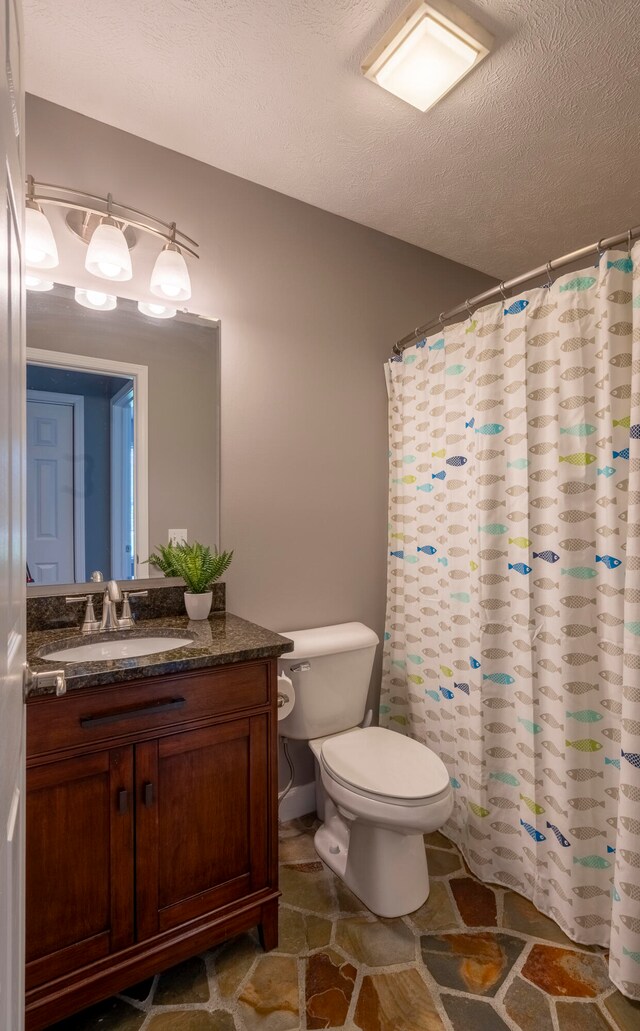 bathroom featuring walk in shower, vanity, a textured ceiling, and toilet