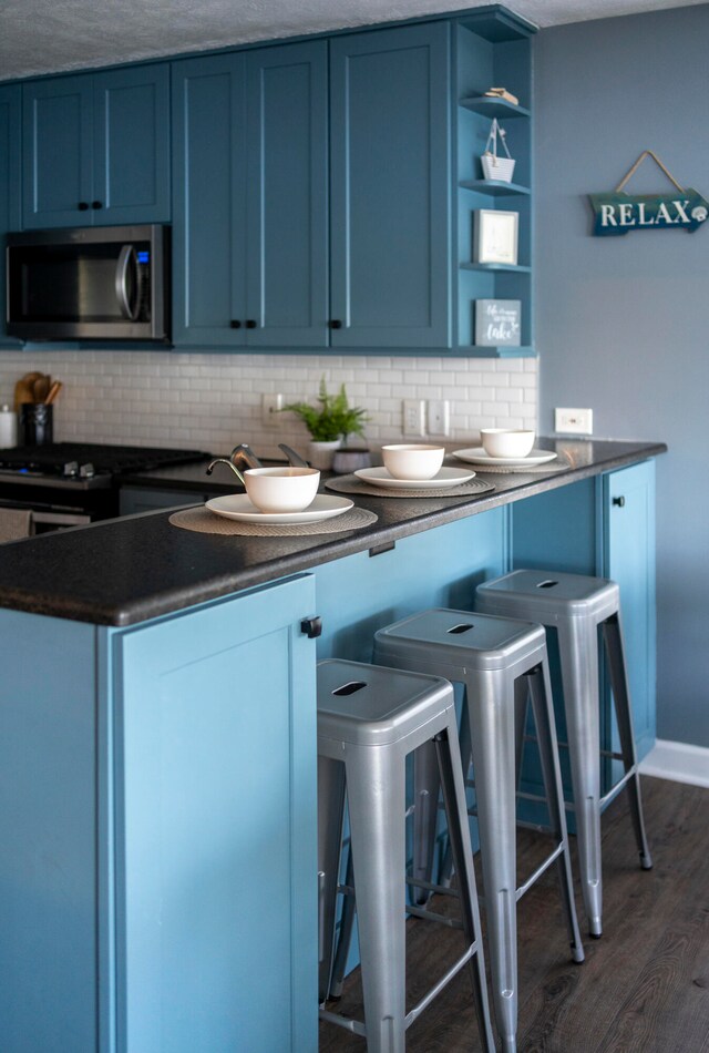 kitchen with decorative backsplash, a kitchen breakfast bar, dark hardwood / wood-style floors, and blue cabinets