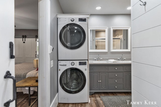 clothes washing area with cabinets, dark wood-type flooring, sink, a barn door, and stacked washer / dryer