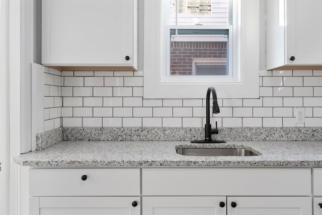 interior details featuring tasteful backsplash, light stone countertops, sink, and white cabinets