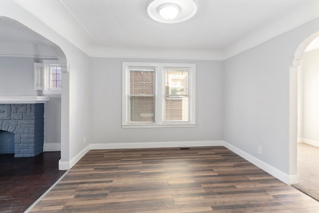 interior space with a stone fireplace, a wealth of natural light, and dark wood-type flooring