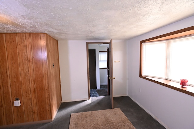 hall featuring a textured ceiling and dark carpet