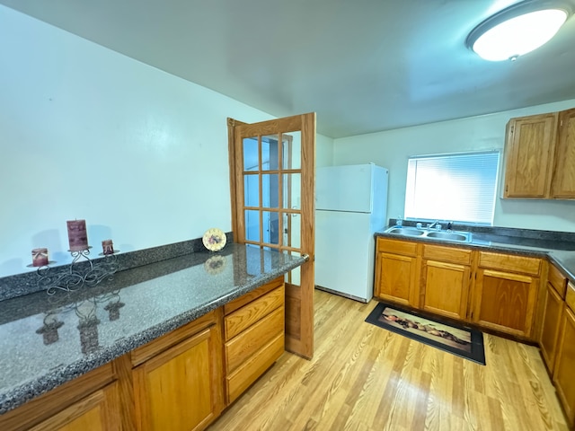 kitchen featuring white refrigerator, light wood-type flooring, sink, and dark stone counters