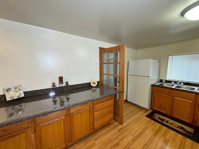 kitchen featuring sink, white fridge, dark stone counters, and light wood-type flooring