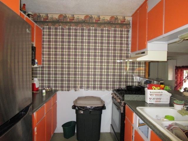 kitchen with a textured ceiling, stainless steel fridge, sink, and black gas range oven