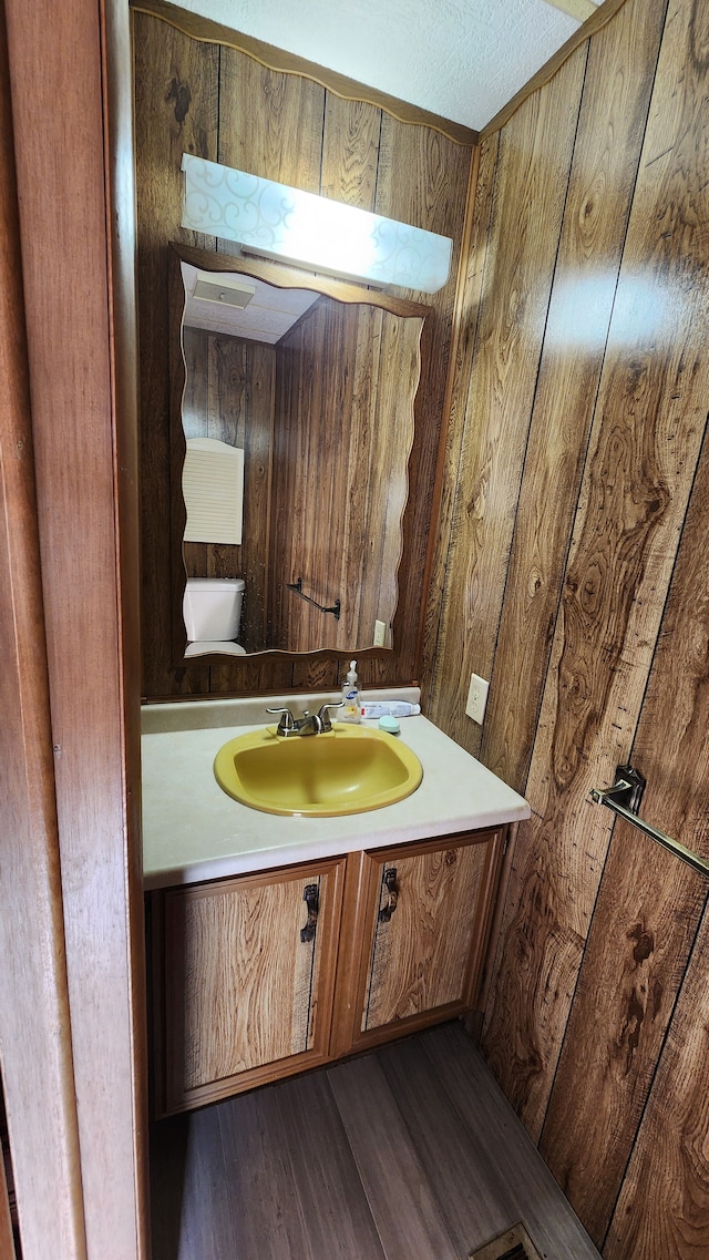 bathroom with wooden walls, hardwood / wood-style floors, vanity, and a textured ceiling