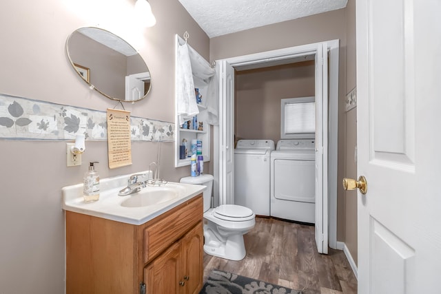 bathroom featuring vanity, a textured ceiling, wood-type flooring, washing machine and dryer, and toilet