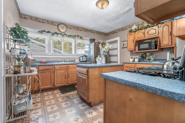 kitchen with a kitchen island, sink, a textured ceiling, and stainless steel refrigerator