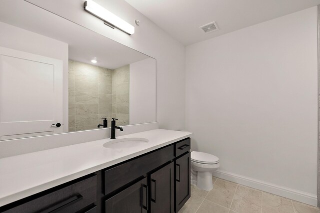 bathroom featuring a tile shower, vanity, and toilet