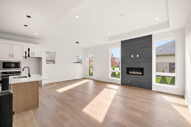 kitchen with a healthy amount of sunlight, white cabinetry, an island with sink, and light hardwood / wood-style flooring