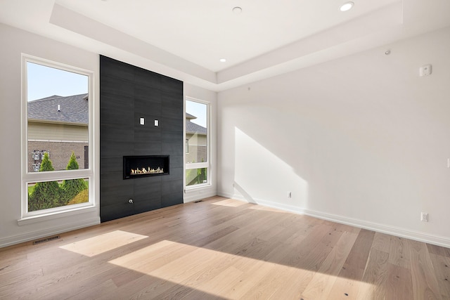 unfurnished living room with light hardwood / wood-style floors, a tray ceiling, and a tiled fireplace