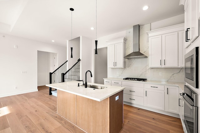 kitchen featuring a kitchen island with sink, white cabinets, wall chimney range hood, sink, and light hardwood / wood-style floors