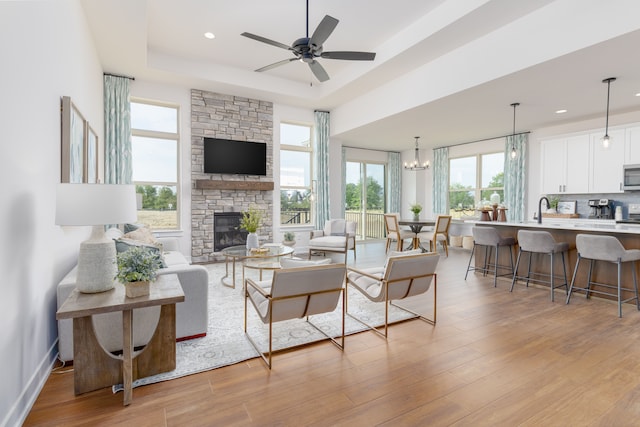 living room with light wood-type flooring, a raised ceiling, a healthy amount of sunlight, and a stone fireplace