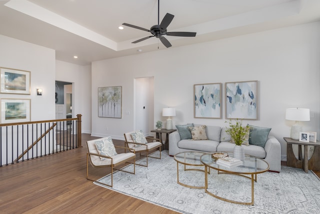 living room with a raised ceiling, ceiling fan, and wood-type flooring