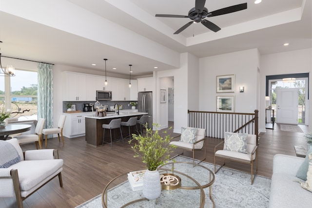 living room with a raised ceiling, dark wood-type flooring, and ceiling fan with notable chandelier