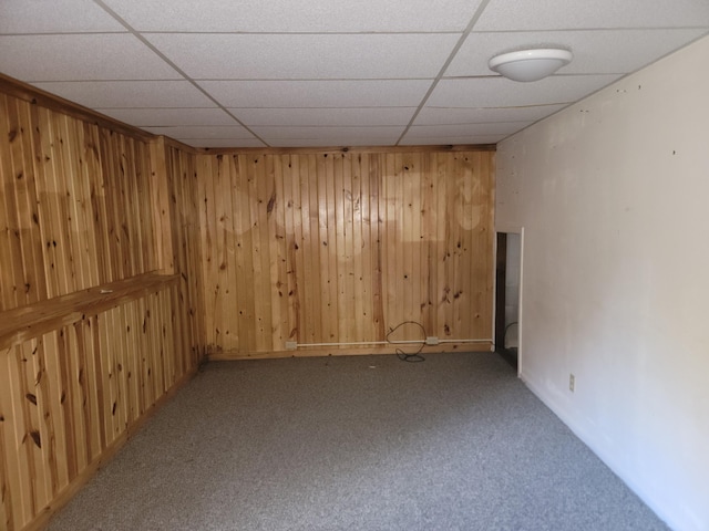 carpeted spare room with a drop ceiling and wood walls