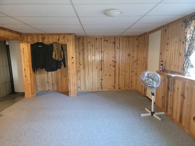 spare room with a drop ceiling, carpet, and wooden walls