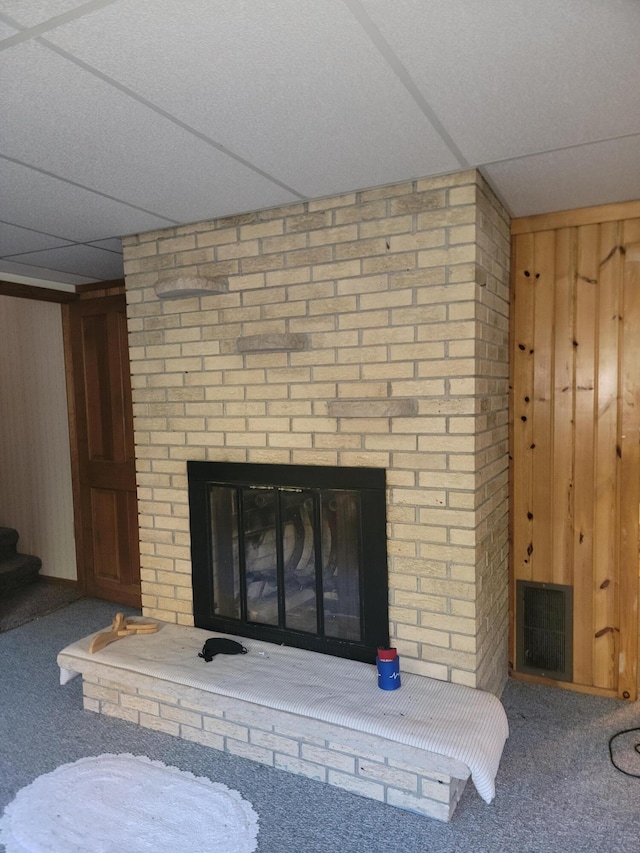 details featuring visible vents, a brick fireplace, a drop ceiling, wood walls, and carpet floors