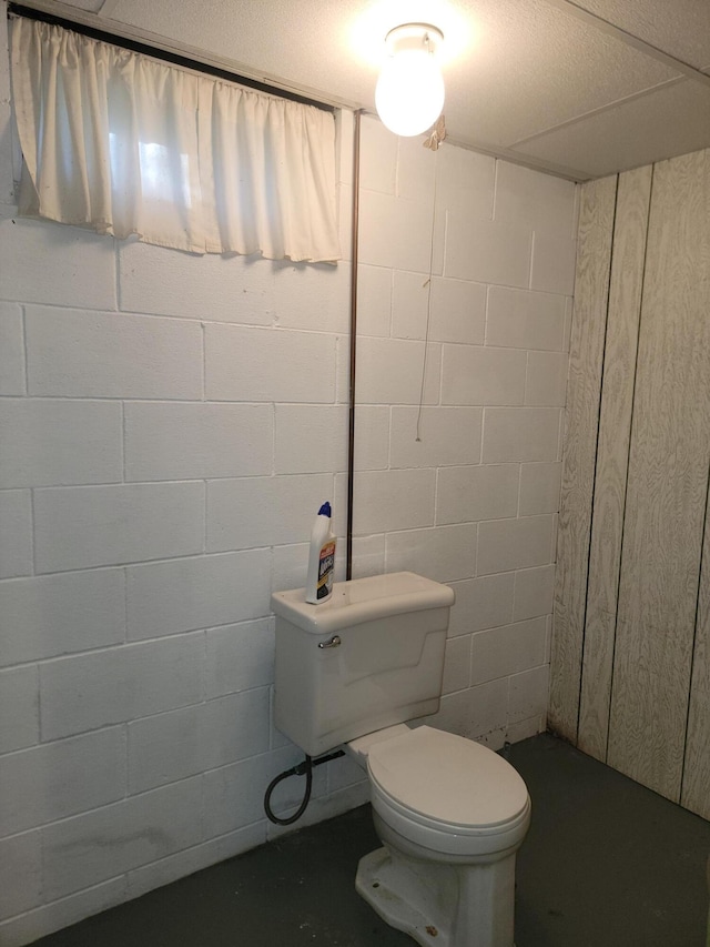 bathroom featuring concrete floors, toilet, and concrete block wall