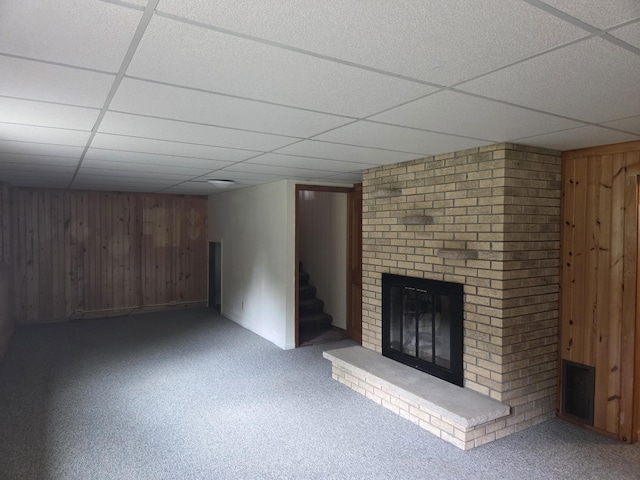 4085 N Cedar Lake Rd, Edmore, MI 48829 - unfurnished living room featuring a drop ceiling, a fireplace, wood walls, stairs, and carpet floors