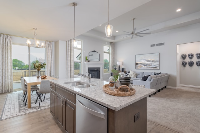 kitchen with dishwasher, ceiling fan with notable chandelier, sink, light stone countertops, and an island with sink