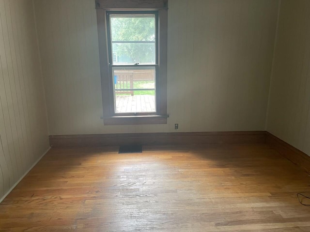 unfurnished room with light wood-type flooring and wooden walls