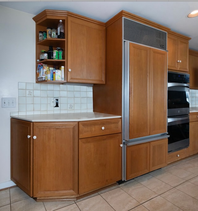 kitchen with tasteful backsplash, paneled built in refrigerator, double oven, and light tile patterned floors