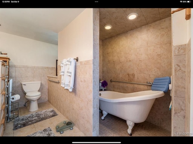 bathroom with toilet, a bathtub, tile patterned floors, and tile walls