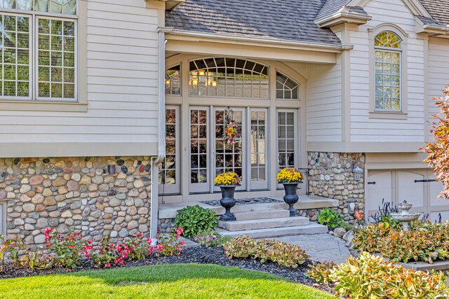 entrance to property with a garage, stone siding, a shingled roof, and french doors