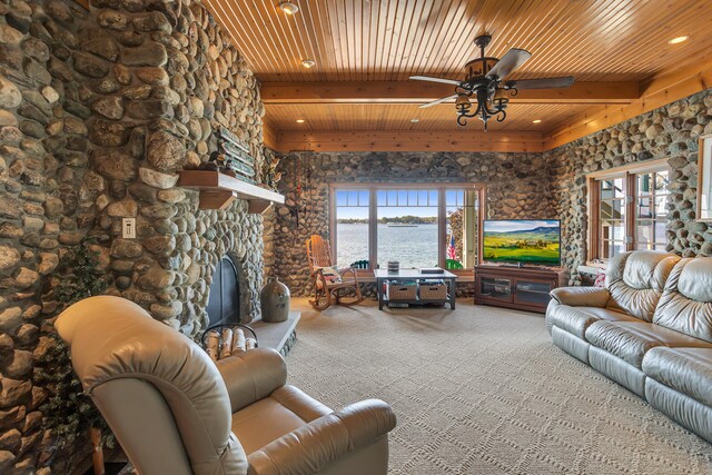 carpeted living area featuring wood ceiling, a stone fireplace, beam ceiling, and a ceiling fan