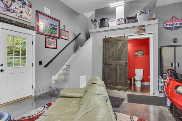 living area with a barn door, visible vents, baseboards, stairway, and concrete floors