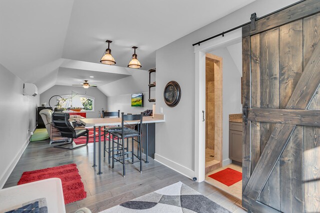 dining space featuring dark wood-style flooring, a wall unit AC, lofted ceiling, a barn door, and baseboards