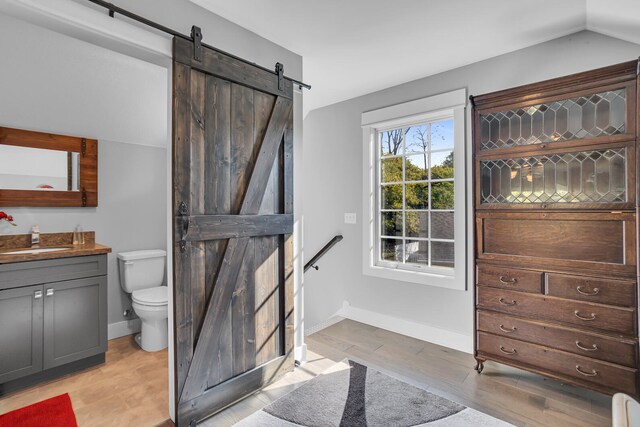 half bath with toilet, wood finished floors, vanity, baseboards, and vaulted ceiling