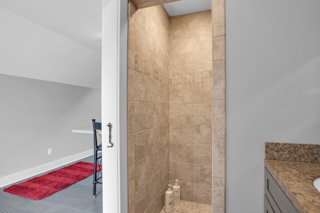 full bathroom with tiled shower, vanity, baseboards, and wood finished floors