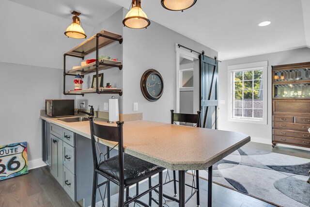 kitchen with a barn door, gray cabinetry, a sink, a kitchen breakfast bar, and light countertops