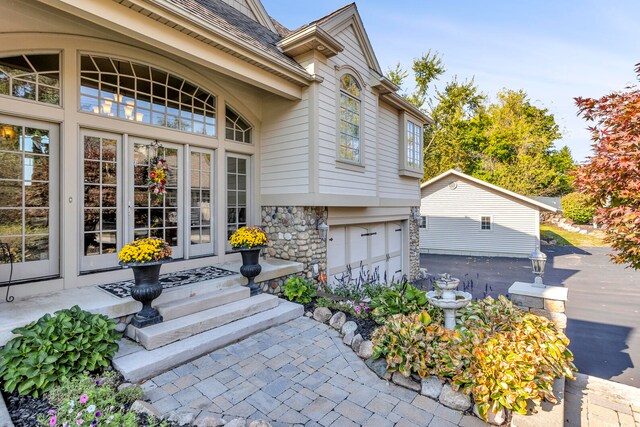 entrance to property featuring stone siding, french doors, and a shingled roof