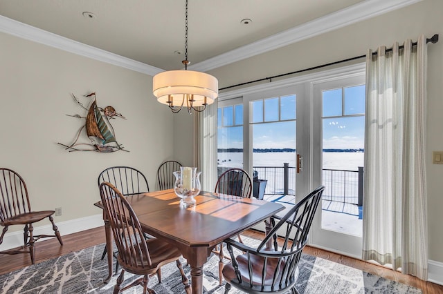 dining area featuring ornamental molding, a water view, wood finished floors, and baseboards