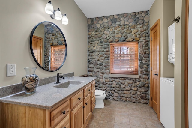 bathroom featuring stacked washer / dryer, tile patterned flooring, vanity, and toilet