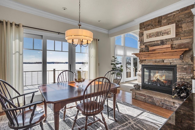 dining room featuring a stone fireplace, a water view, wood finished floors, and crown molding