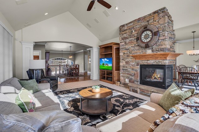 living area featuring decorative columns, arched walkways, crown molding, a fireplace, and high vaulted ceiling